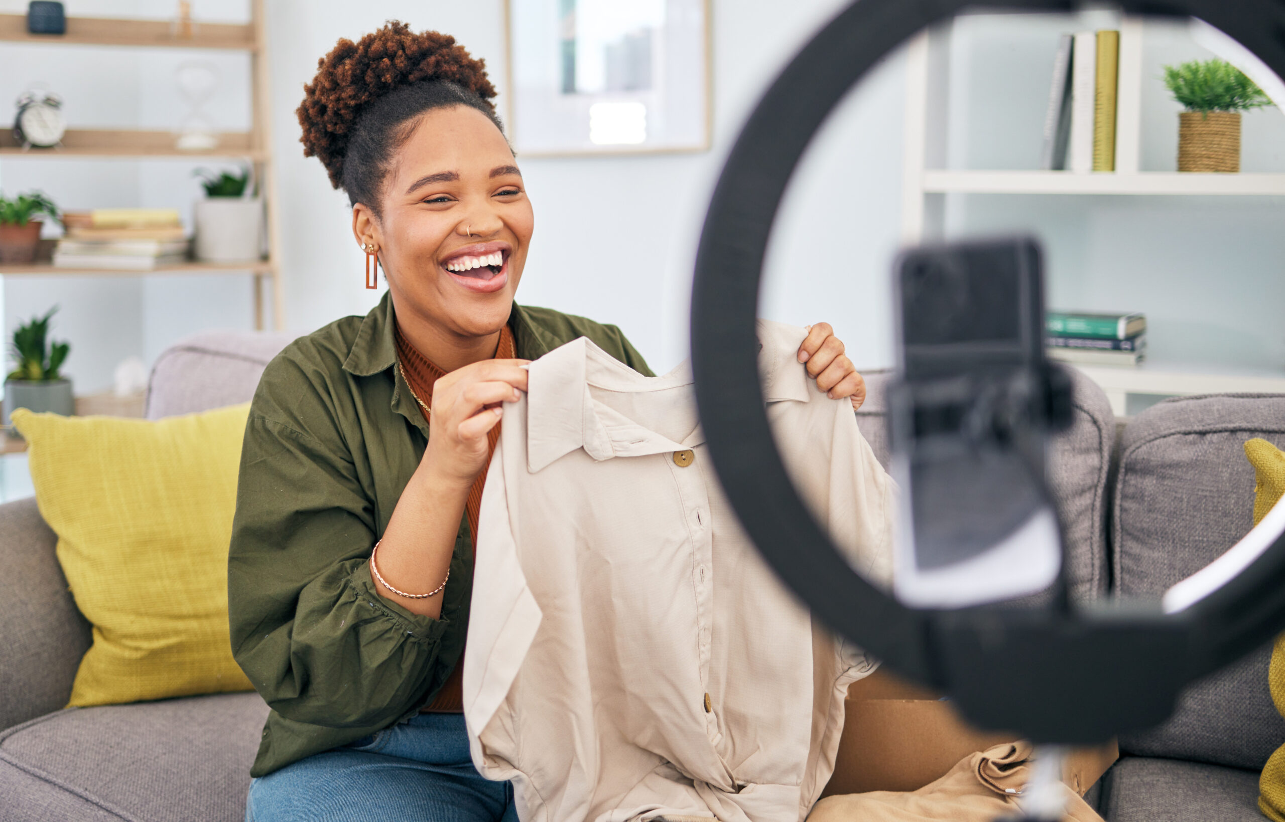 Fashion, live streaming and a black woman content creator unboxing a clothes outfit in her home. Social media, brand deal and a happy female influencer recording a broadcast for subscription service.