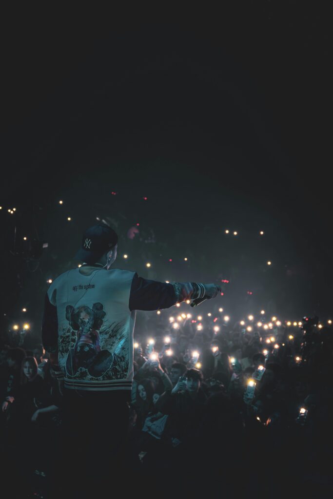 Performer on stage facing a vibrant crowd holding lights during a night concert.