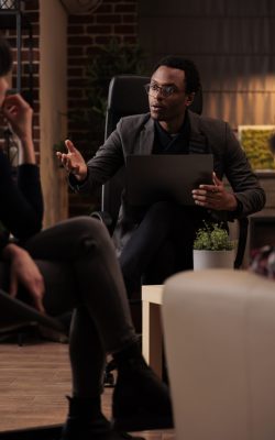 Young psychotherapist explaining psychological issues to people at couple therapy, using laptop to take psychoanalysis notes. Listening to conflict and finding solution to save marriage.